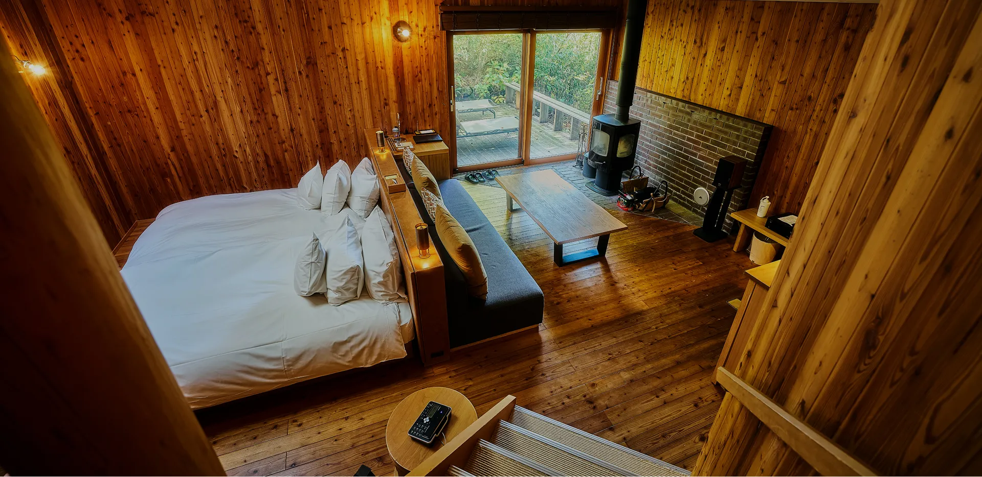 緑に包まれた木造の宿泊施設、窓から明かりが漏れる外観