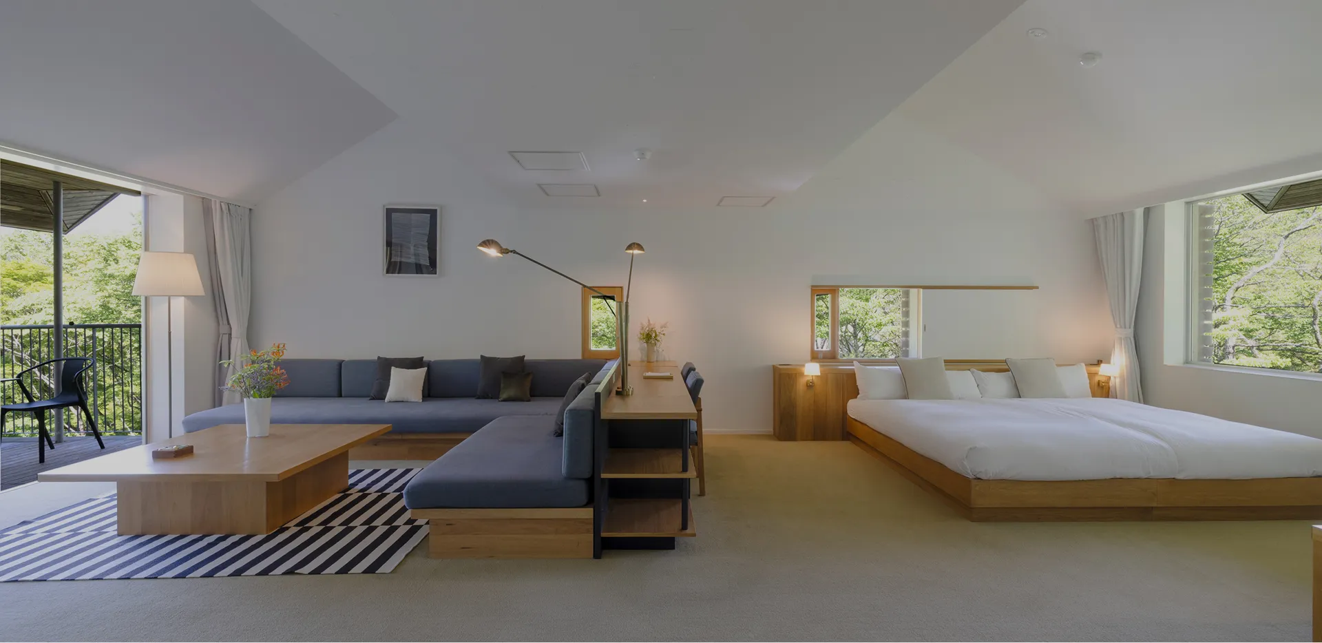 大きな窓から自然を望む客室、暖炉とテーブル、ベッドのある落ち着いた空間