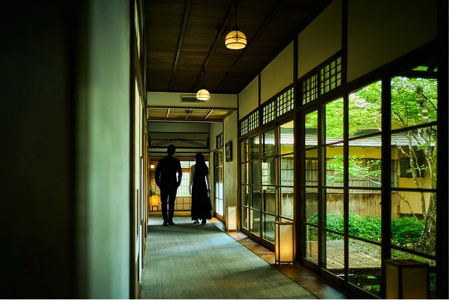 ガラス張りの廊下から外の緑を眺められる館内通路